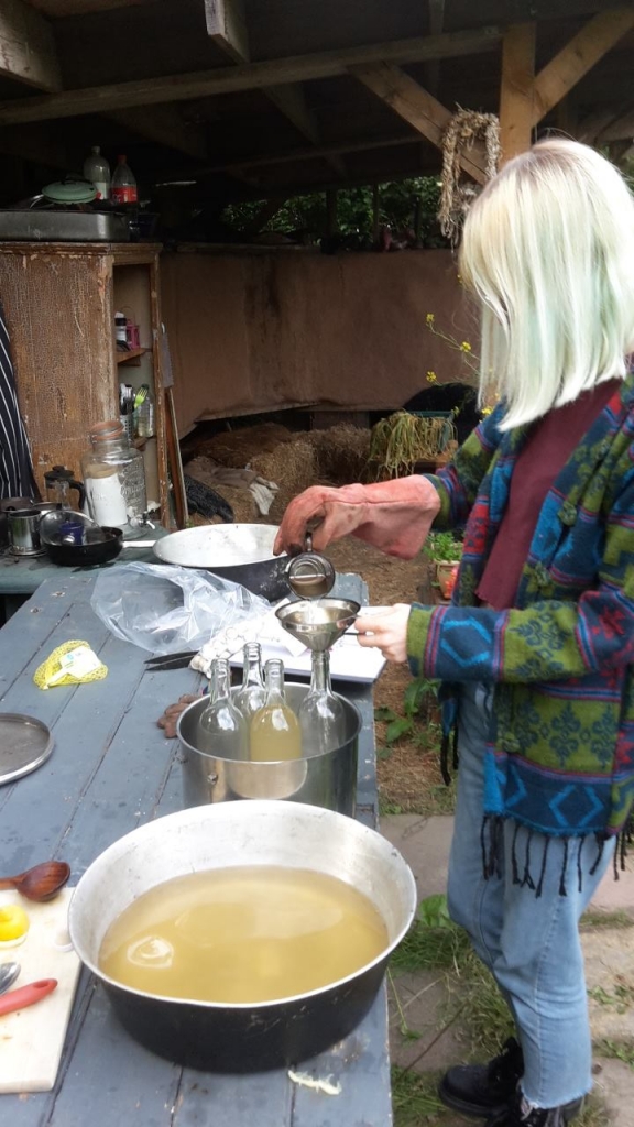 A person decanting elderflower juice into glass bottles.
