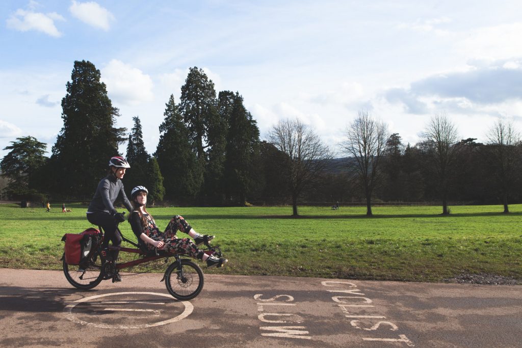 two women ride tandem on a bike with green fields behind them